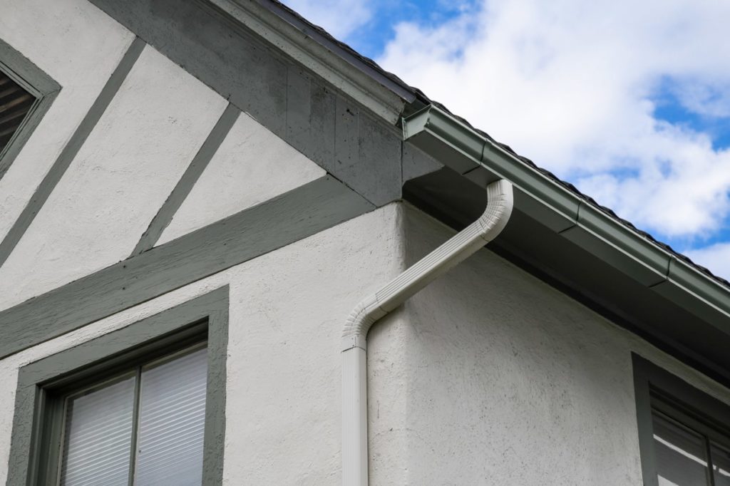 Custom rain gutters with downspouts on a green and tan home